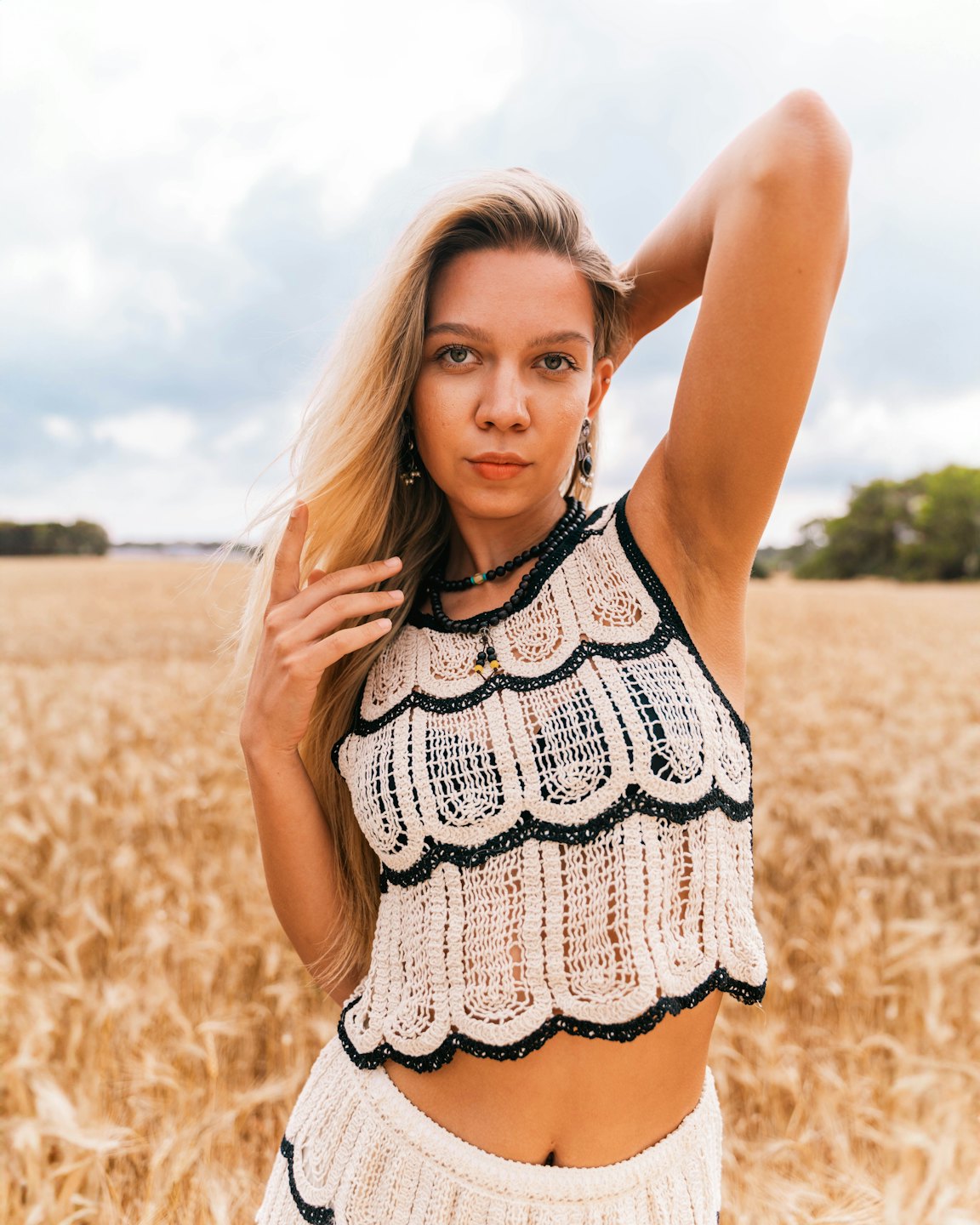 Woman in a crocheted outfit stands in a wheat field.