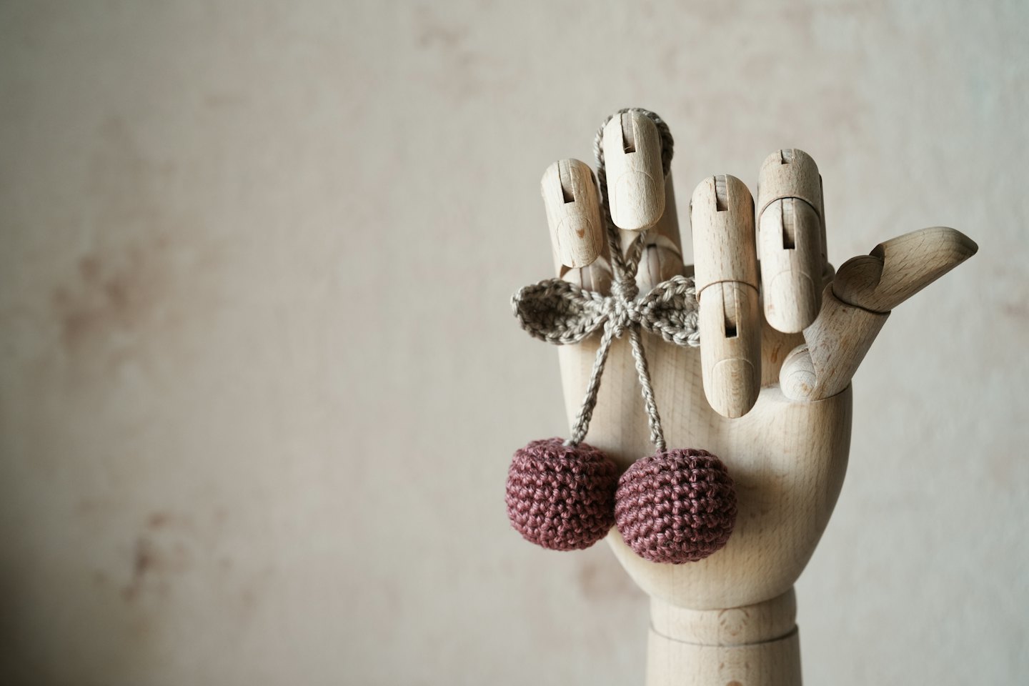 Wooden hand holding a crocheted cherry decoration.