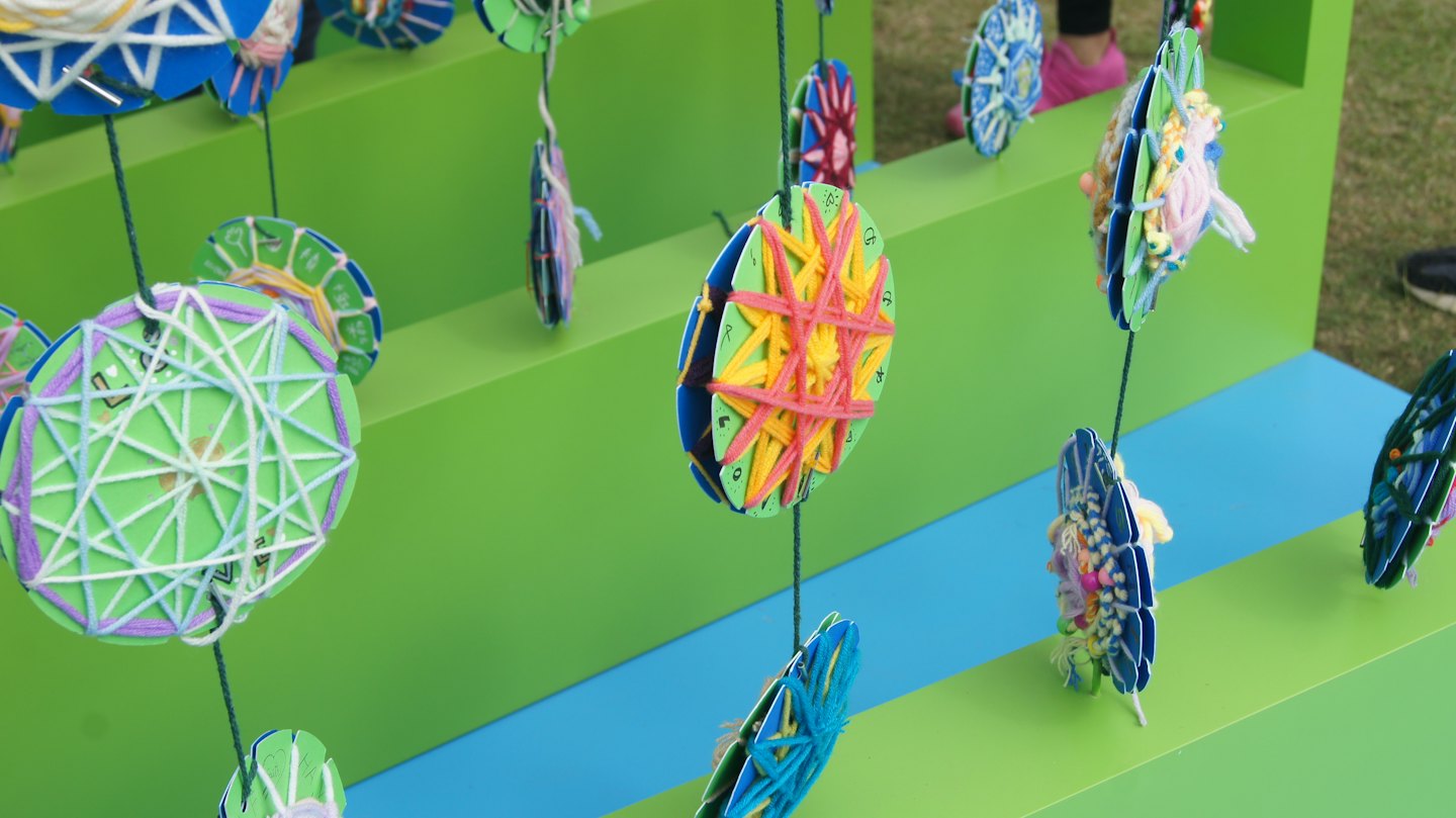 Colorful yarn art pieces hang from a garden display stand.