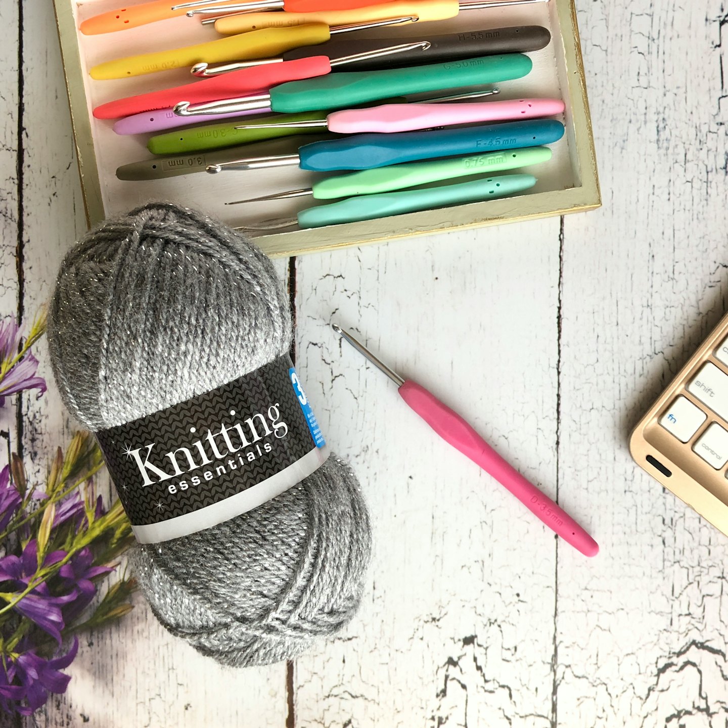 Silver yarn, pink crochet hook, and colorful hooks in wooden tray.