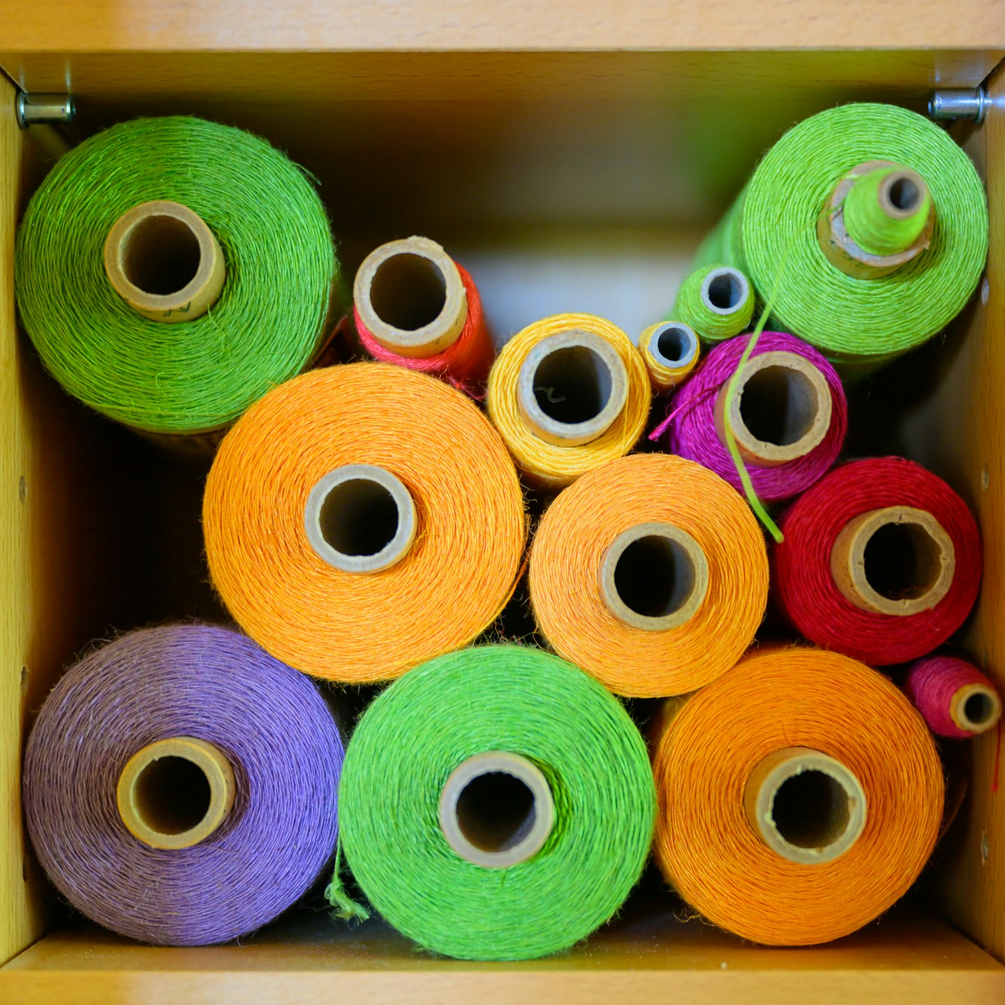 Colorful spools of thread arranged neatly in a wooden drawer.